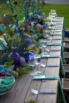 a long table is set with empty wine glasses and place settings for an outdoor dinner