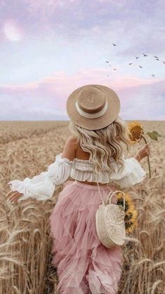 a woman in a pink dress and straw hat walking through a field with a sunflower