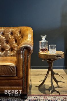 a leather chair and table with two glasses on it in front of a blue wall