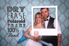 a man and woman posing for a photo in front of a wall with the words dry erase polaroid frame 100 % wool