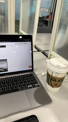 an open laptop computer sitting on top of a white table next to a cup of coffee