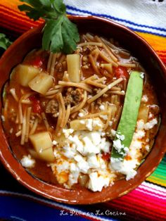 a bowl filled with pasta and vegetables on top of a colorful table cloth next to a spoon