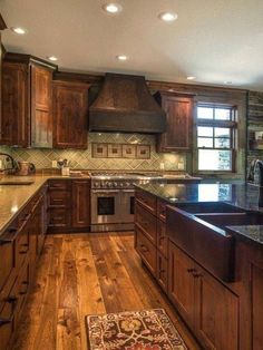 a large kitchen with wooden cabinets and granite counter tops, hardwood flooring and an area rug in front of the sink