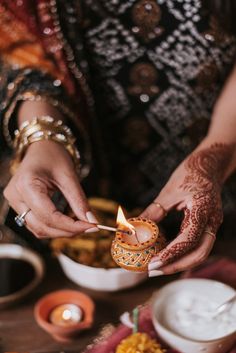 a woman holding a lit candle in her hand while sitting at a table filled with food