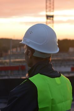 a man wearing a safety vest and hard hat looking at the sunset over a construction site