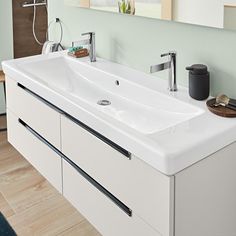 a bathroom sink with two faucets and a mirror above it, in front of a wooden floor