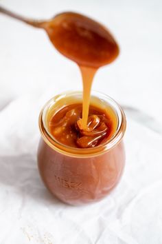 a spoon pouring caramel sauce into a jar