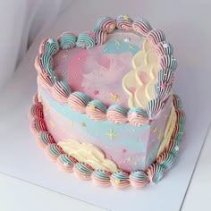 a heart shaped cake with pastel icing and stars on the top is sitting on a white surface