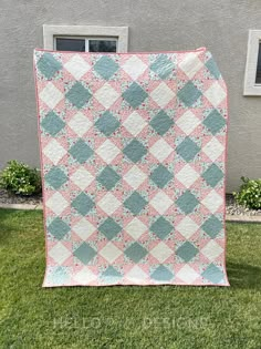 a pink and blue quilt sitting on top of a green grass covered field next to a building