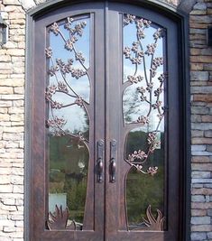 a large wooden door with glass panels and flowers on the side walk next to a brick building