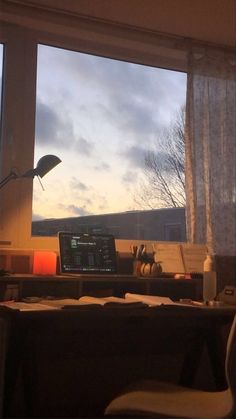 a laptop computer sitting on top of a wooden desk in front of a large window