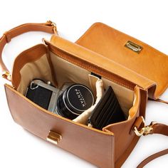 an open brown leather bag with various items inside it on a white surface, including a camera and cell phone