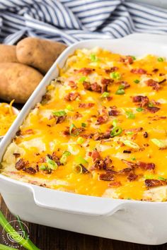 a casserole dish with potatoes and bacon in it on a wooden table next to some green onions