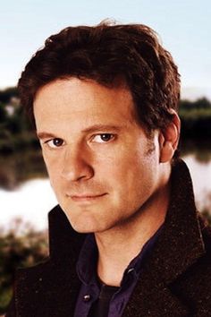 a man with brown hair and blue eyes standing in front of a body of water