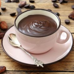 a pink cup filled with chocolate on top of a saucer next to coffee beans