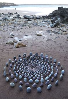 a group of rocks arranged in the shape of a spiral on a beach with water and sand behind them