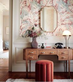 a desk with a mirror, stool and flowers on it in front of a wall