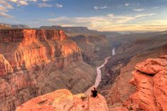 a man sitting on the edge of a cliff overlooking a river and canyon below him