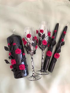 three wine glasses with red roses on them are sitting next to two black candles and one is empty