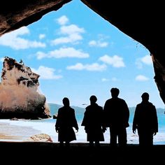 four people standing in front of a cave looking out at the ocean