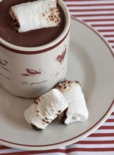 two marshmallows are on the plate next to a cup of hot chocolate