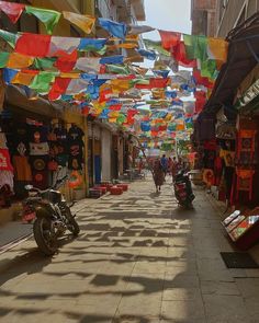 people walking down an alley lined with shops and colorful flags hanging from the buildings on both sides