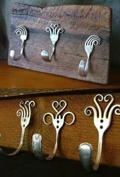 several metal spoons and forks are on a wooden shelf next to a box with hooks