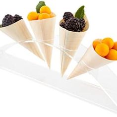 four cones filled with fruit on top of a white counter next to oranges and blackberries