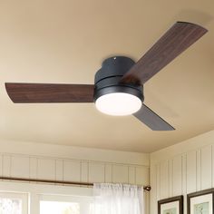 a ceiling fan in a living room with pictures on the wall and window behind it