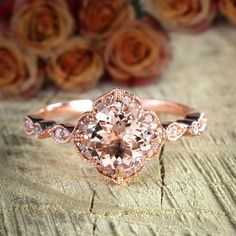 a pink diamond ring sitting on top of a wooden table next to some rose petals