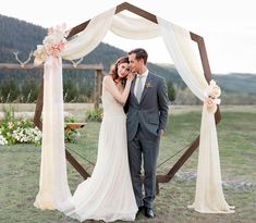 a bride and groom standing under an arch decorated with flowers