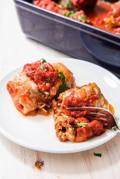 a white plate topped with lasagna covered in marinara sauce next to a casserole dish