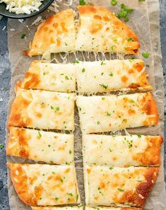 sliced pizza sitting on top of a piece of parchment paper next to a bowl of cheese