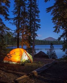 a tent pitched up in the woods at night near a lake with mountains and trees