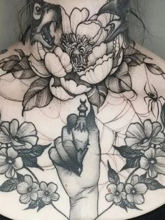 a woman's back with flowers and birds on her neck, holding the peace sign