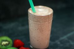 a smoothie in a glass with a green straw next to kiwis and raspberries