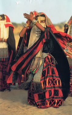 a group of people dressed in costumes and headdress walking through the desert with their hands together