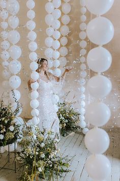 a woman in a white dress is surrounded by balloons and greenery on the floor