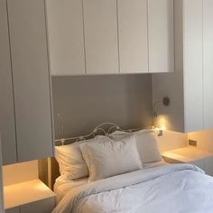 a bed with white linens and pillows in a room that has built - in shelving