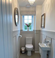 a white toilet sitting next to a sink in a bathroom under a window with a mirror above it