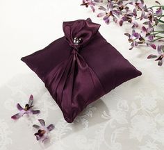 a small purple bag with a bow on the side and flowers in front of it