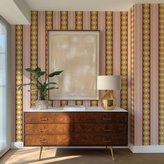 a dresser with a lamp and a painting on the wall behind it in front of a window