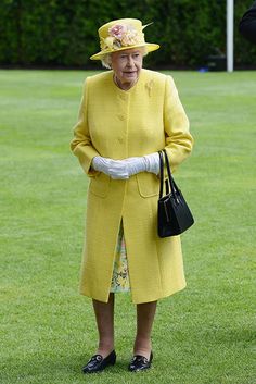 an older woman in yellow coat and hat standing on the grass with her handbag