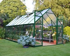 a green house sitting in the middle of a lush green field with lots of flowers