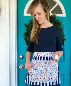 a woman standing in front of a blue door holding an item with one hand and looking down at it