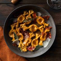 pasta with bacon and cheese in a bowl on a wooden table next to a glass of wine