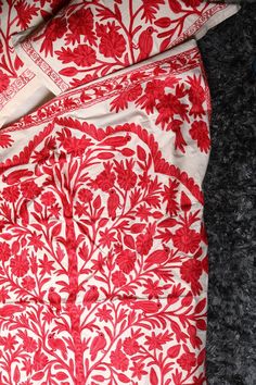 a red and white bed spread on top of a black carpeted floor next to a pillow