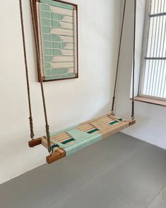 a wooden swing hanging from the side of a white wall next to a window with blinds on it