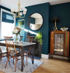 a dining room with blue walls and wooden furniture in the center, along with a large round mirror on the wall