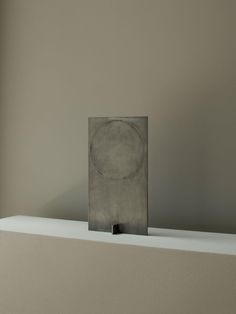 a square metal object sitting on top of a white shelf in front of a window